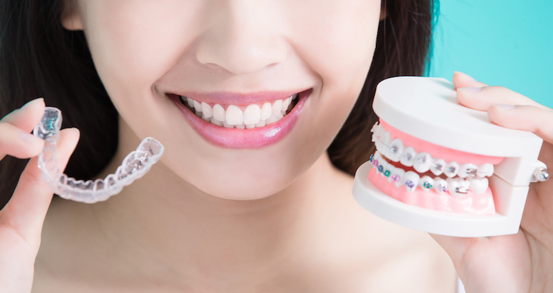 girl holding both an invisalign aligner and a metal brace