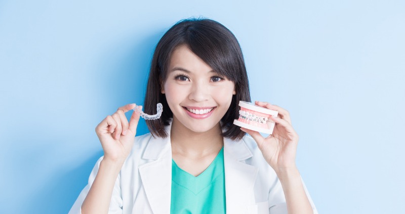 Female orthodontist holding an Invisalign aligner and jaw mould with braces and checking is invisalign better than braces
