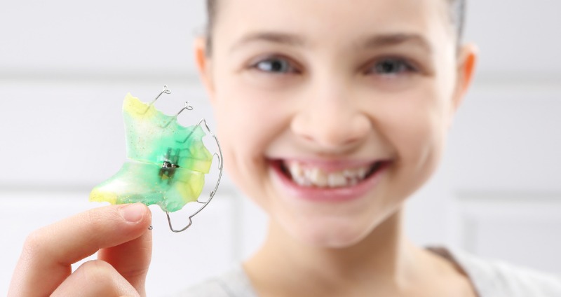a young girl holding her orthodontist plate and smiling