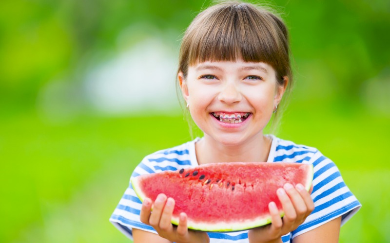 young girl with dental braces holding watermelon and smiling