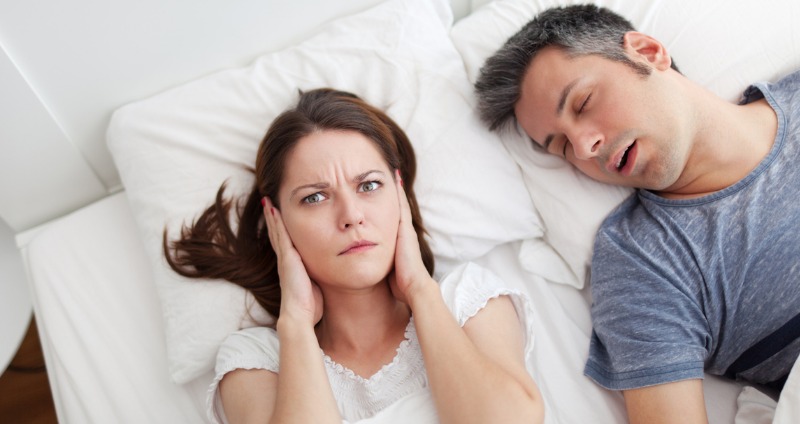 Lady laying in bed blocking her ears from snoring partner 