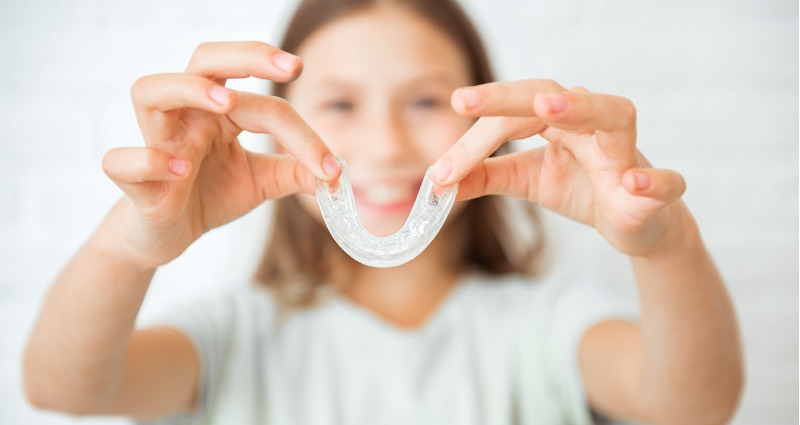 A child holding up her Invisalign retainer to the camera