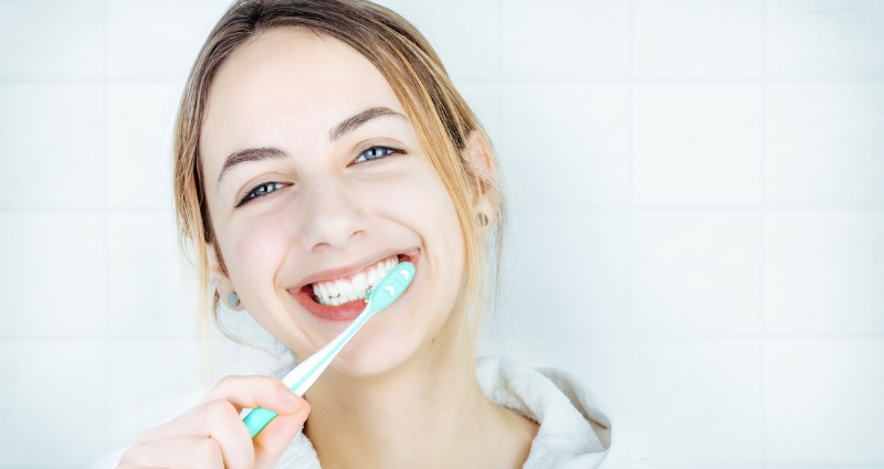 Young teenage girl smiling brushing her teeth properly 