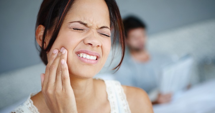 Woman expressing discomfort while touching her face due to bad teeth and health.