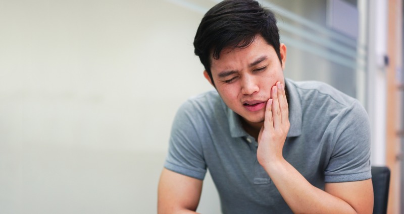 Teenage male suffering from jaw pain caused by teeth grinding