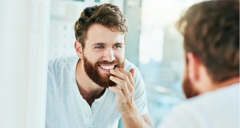 Young male adult smiling at the mirror and looking at his white teeth.