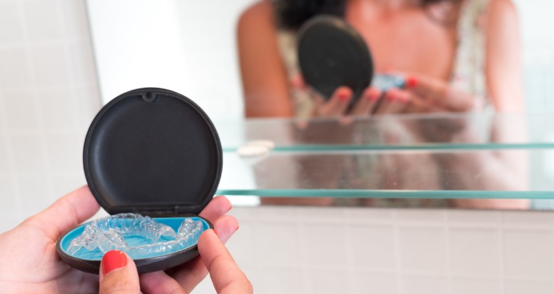 Woman in front of the bathroom mirror, taking her retainers out of their case to wear.