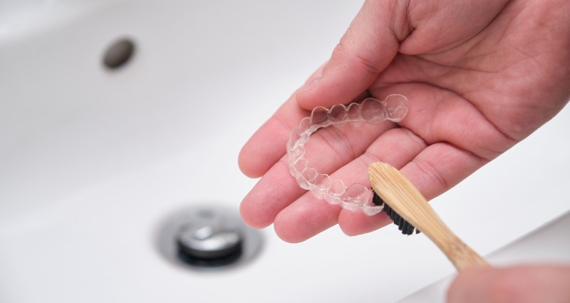 An orthodontic patient cleaning their Invisalign with a toothbrush.
