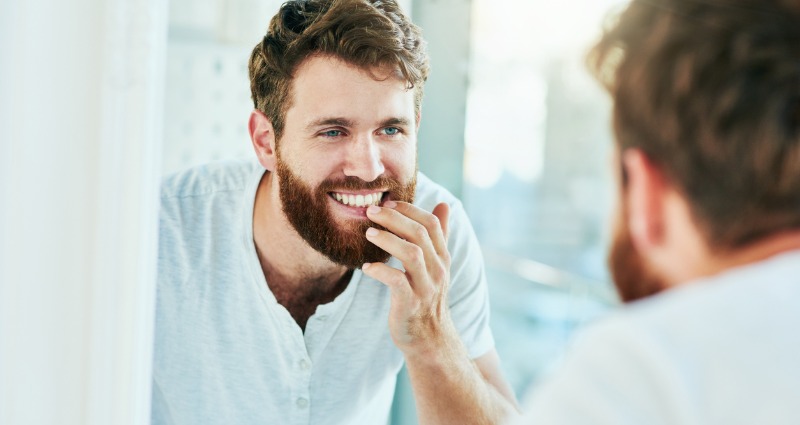 Man in his bathroom inspecting his sensitive teeth in front of the mirror