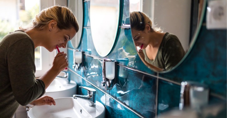 woman brushing her teeth over the bathroom sink